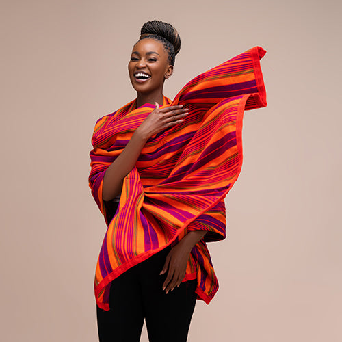 A Black woman posing and smiling while while draped in an orange and red blanket.